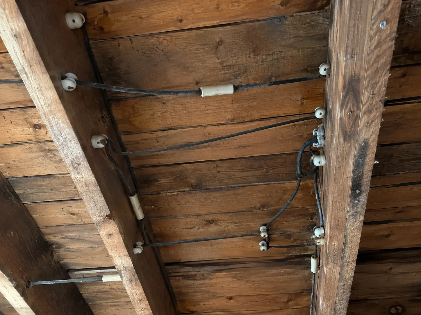 Old knob and tube electrical wiring with ceramic insulators and black conductors mounted to wooden framing