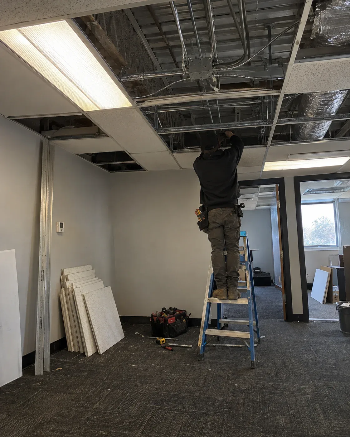 Electrician working on a ladder in a commercial ceiling area in Ajax