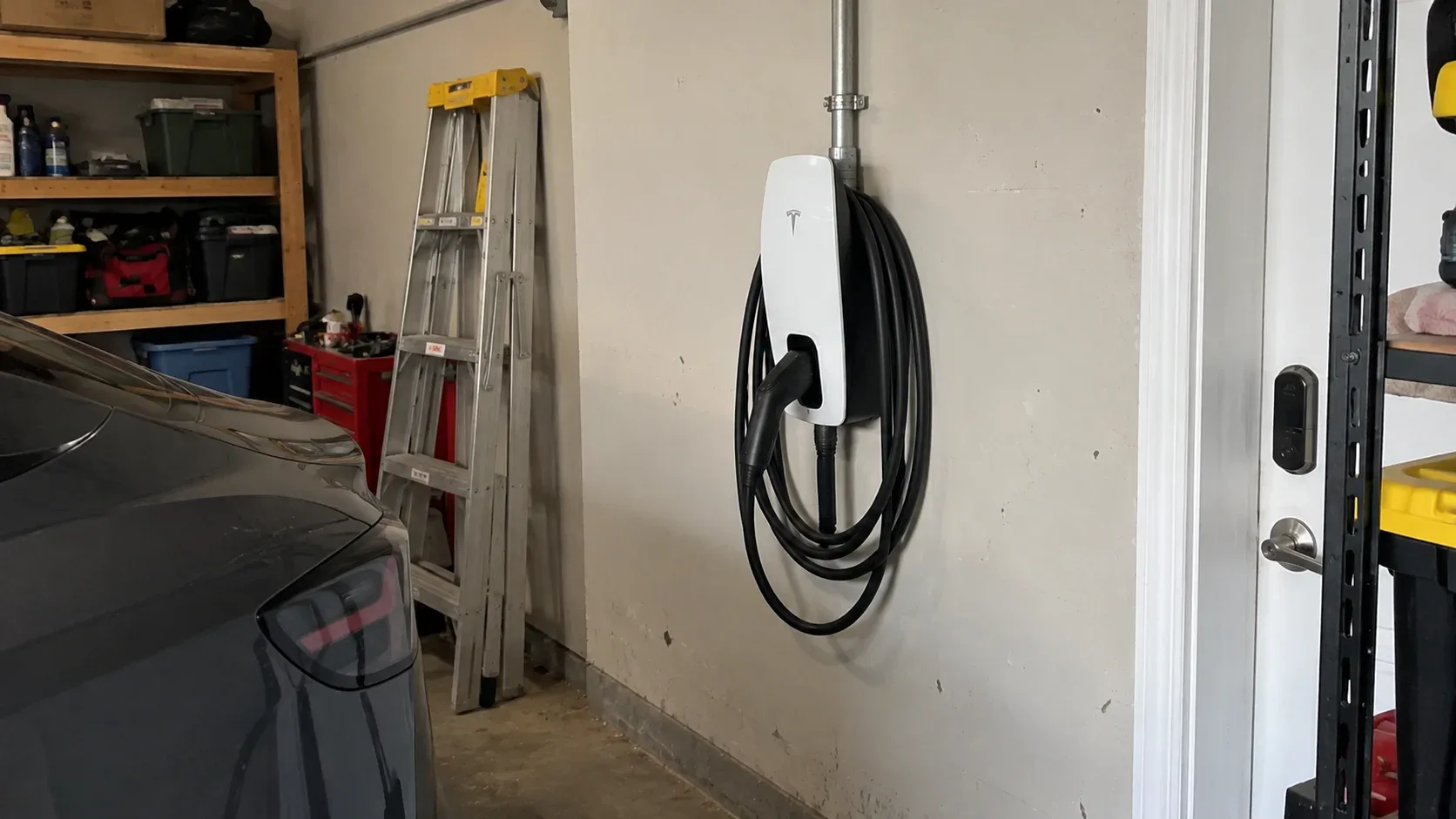 Tesla Wall Connector installed on a garage wall with charging cable connected to an electric vehicle